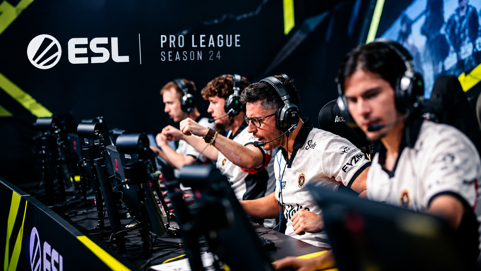 ESL Pro League Season 24 esports players competing at gaming stations on a dark, neon-lit tournament stage.