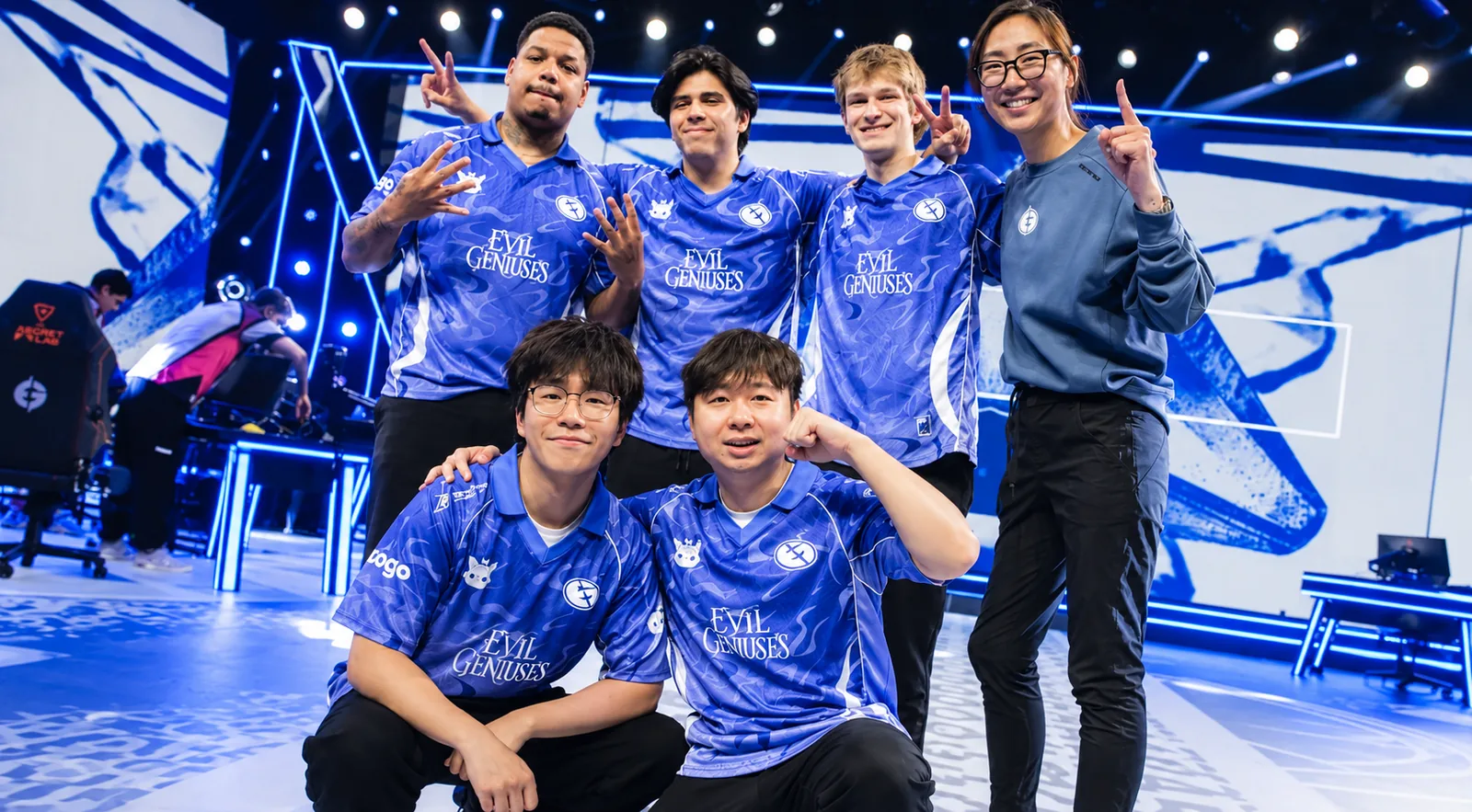 Evil Geniuses esports players and staff posing together in blue team jerseys on a brightly lit competitive gaming stage.