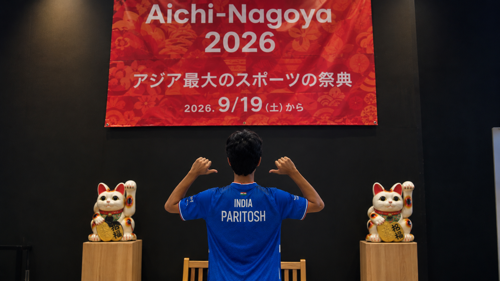 Indian esports player Paritosh seen from behind wearing an India jersey at the Aichi-Nagoya 2026 Asian Games venue, standing between two Japanese lucky cat statues.